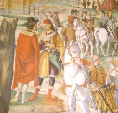 The picture is a part of a fresco in the church of St. Antony of Padua. The fresco made from Filippo Da Verona, 1510. We can se a siege of Padua in 13th century but the soldiers were dressed and armed as the armies of 1500. Among them , there are various exotic warriors. In the middle of the picture we can see a Stratioti with a long red vestment wearing also his black hat; he is speaking with a Janissary who wears on his head the characteristic hat of Hatzi Bectas in a red color. Also we can see other Greek Stratioti with the same vestments ridding horses and bearing their lances with their characteristics small flags on them. 